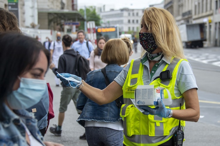 Eine Mitarbeiterin der Basler Verkehrs-Betriebe BVB verteilt Schutzmasken am Bahnhof. Foto: Georgios Kefalas  KEYSTONE  dpa