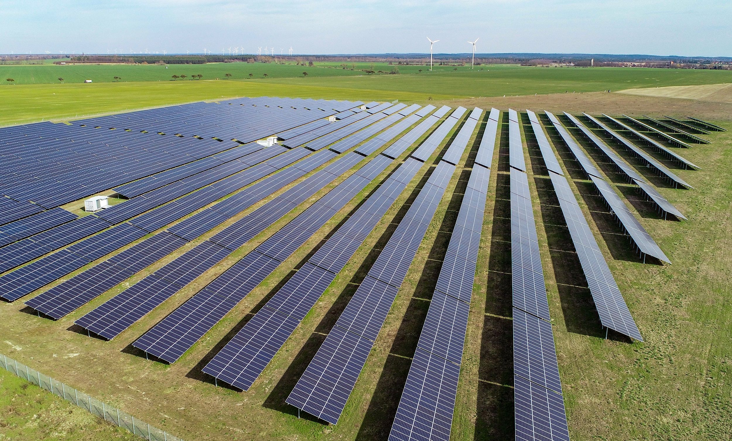 Neue Versorgung: Solar-Anlagen auf landwirtschaftlicher Freifläche, im Hintergrund stehen Windkraftanlagen. Foto: dpa/Pleul