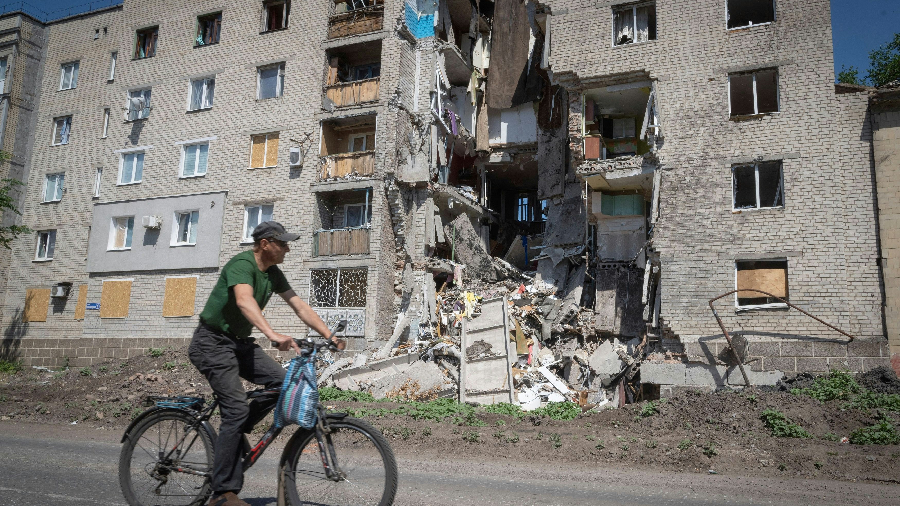 Ein Mann fährt mit dem Fahrrad an einem durch russischen Beschuss beschädigten Gebäude vorbei. Foto: dpa