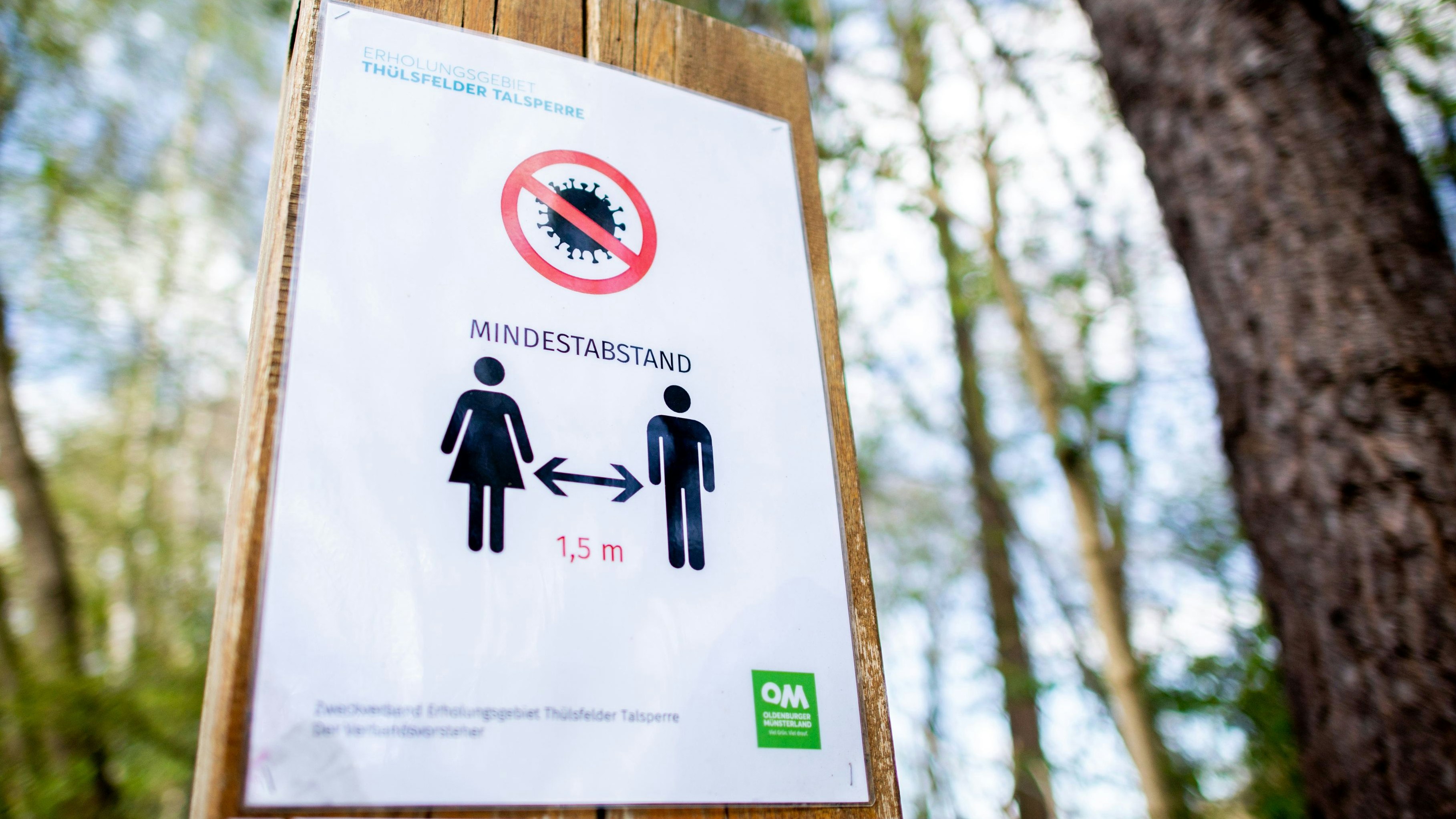 Ein Schild mit der Aufschrift „Mindestabstand“ und einem Piktogramm hängt auf einem Parkplatz an der Thülsfelder Talsperre im Landkreis Cloppenburg. Foto: dpa