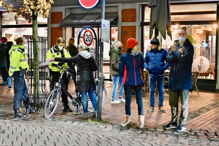 Beamte im  Einsatz: Polizisten kontrollieren Spaziergänger auf der Großen Straße in Vechta. Ein Teilnehmer streckt dem Fotografen seinen Mittelfinger entgegen. Foto: M. Niehues