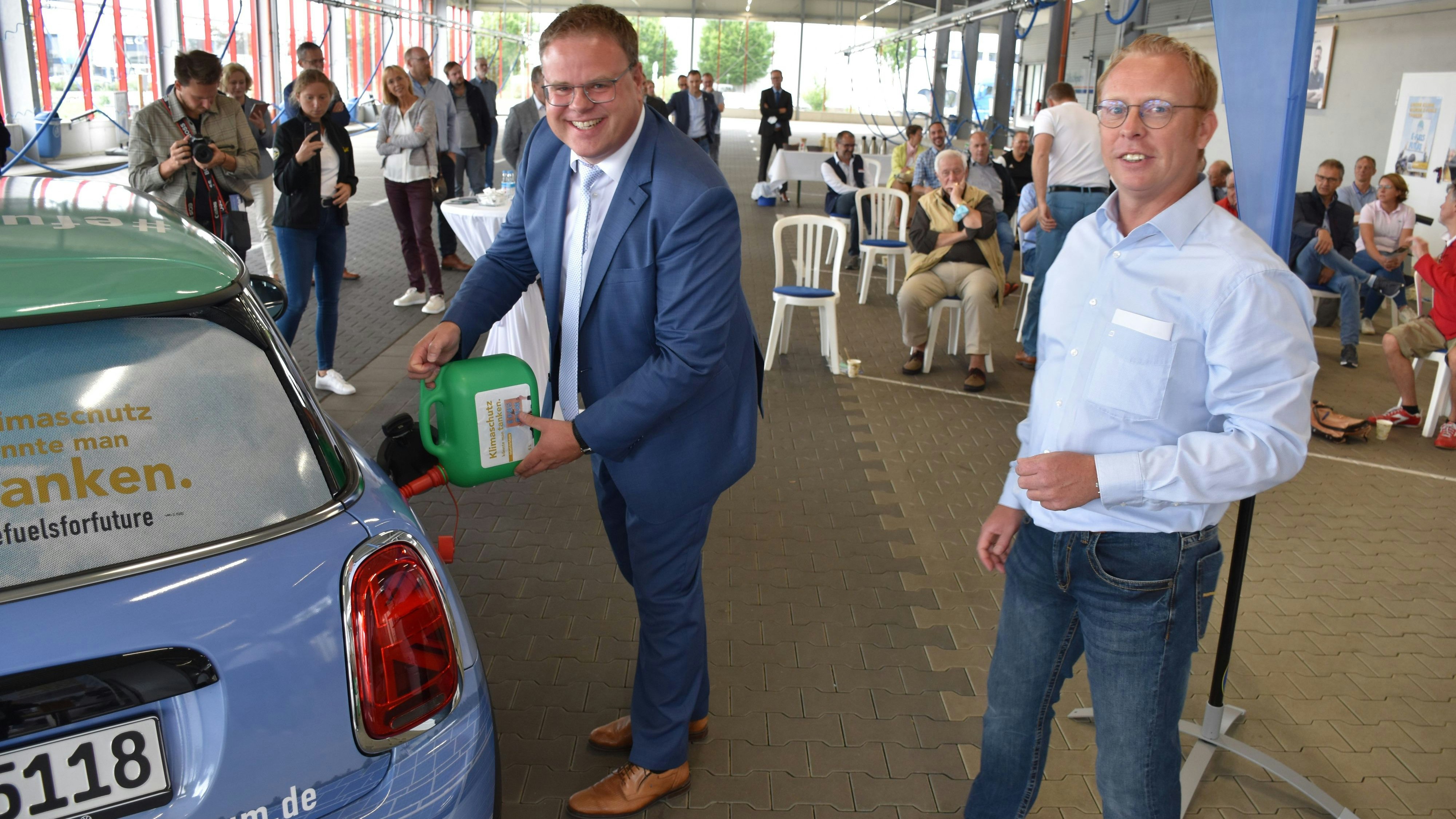 Der BMW „Mini“ fährt anstandslos auch mit synthetischen, grünen Kraftstoffen. Das Auto wurde von Lohnes Bürgermeister Tobias Gerdesmeyer (links) und Marcus Feldhaus betankt. Foto: Kühn