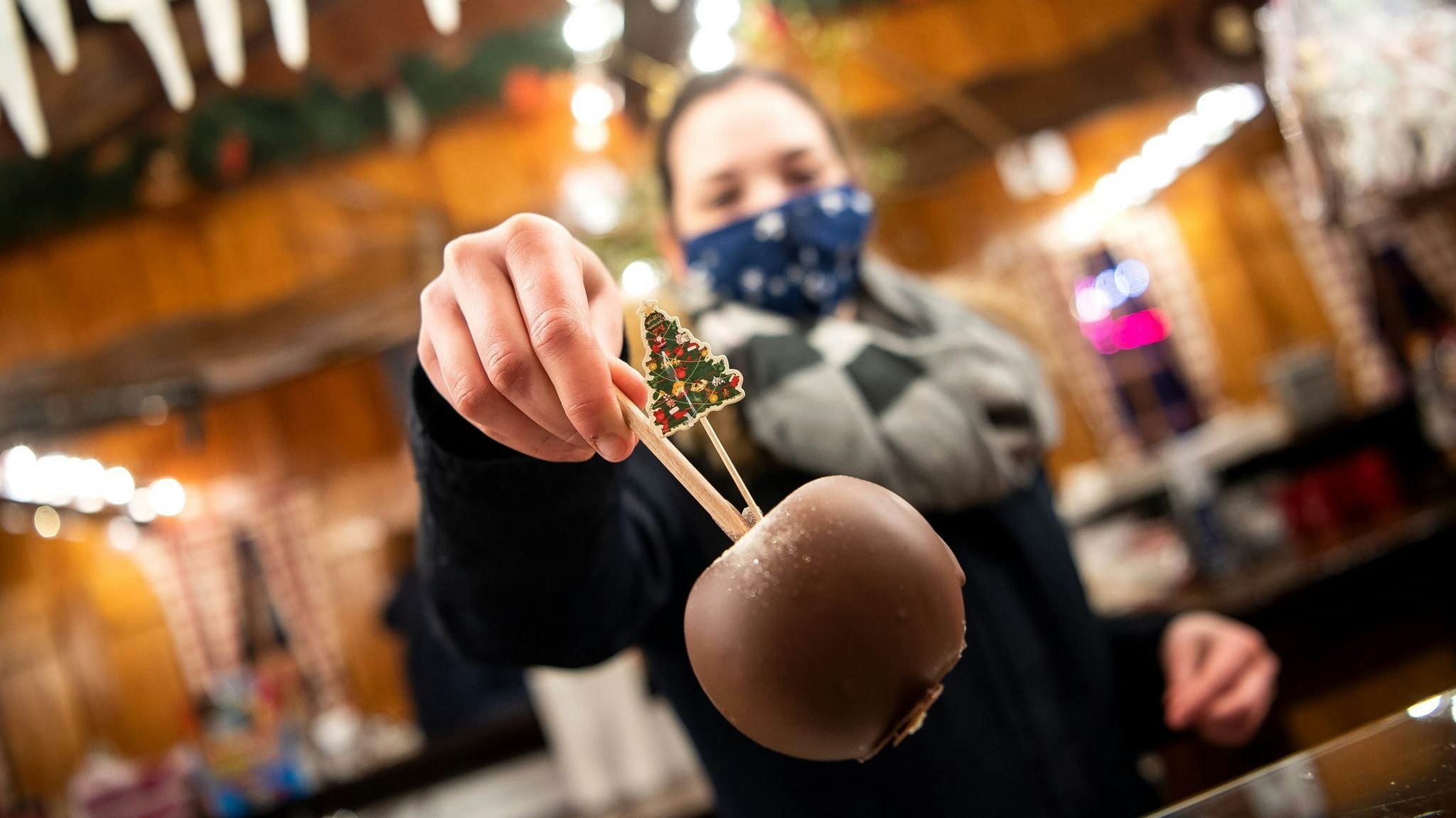 Ein Schokoladenapfel wird über den Tresen eines Weihnachtsstandes gereicht. Foto: dpa/Schuldt
