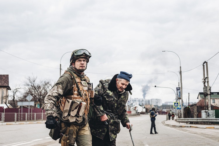Ein ukrainischer Soldat in Irpin hilft einem älteren Mann, die Straße zu überqueren. Foto: dpa