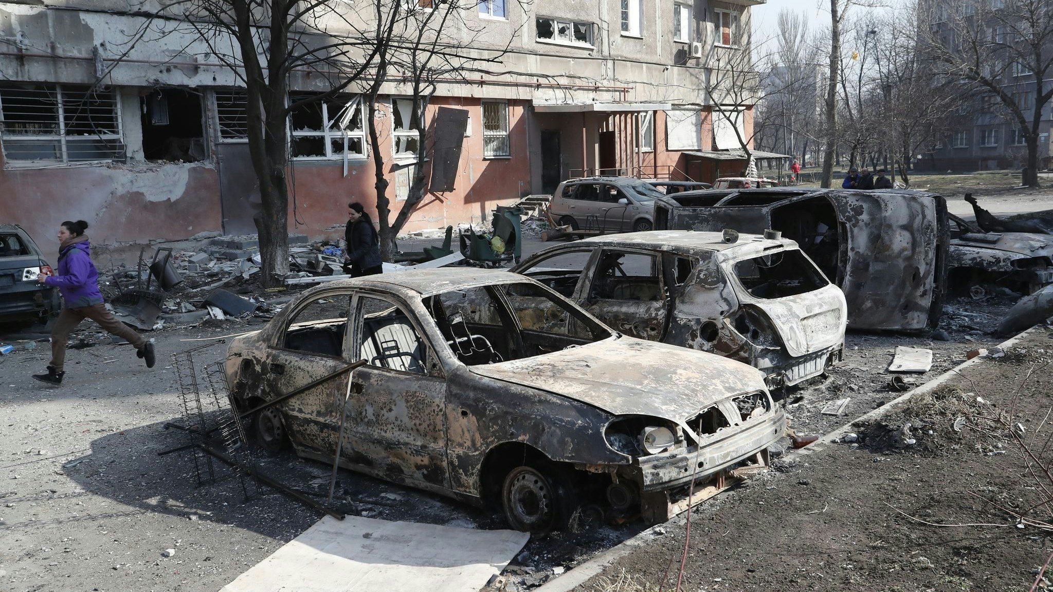 Menschen gehen an zerstörten Autos und Trümmern in Mariupol vorbei. Foto: dpa