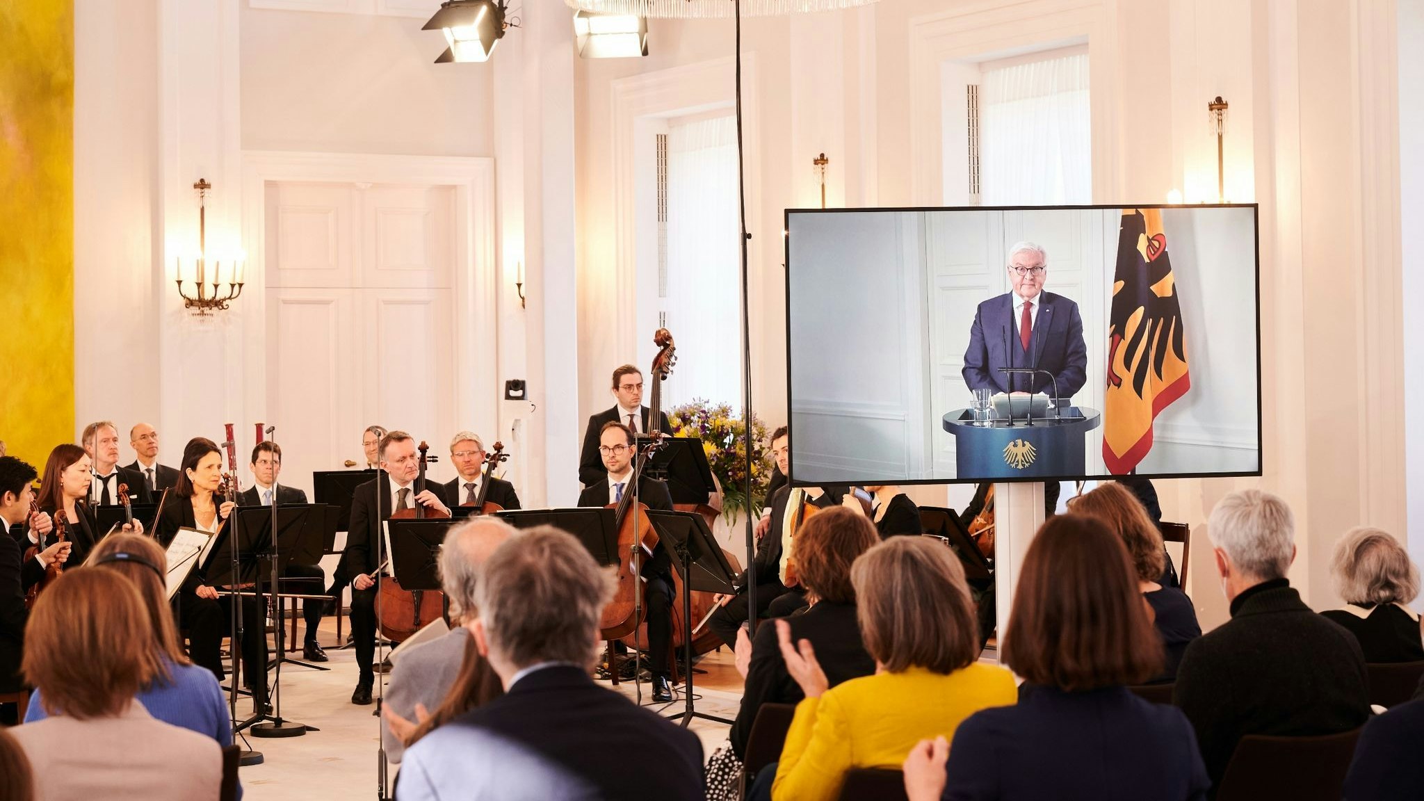 Die Berliner Philharmoniker sitzen im Schloss Bellevue vor ein paar Dutzend Zuschauern während Bundespräsident Frank-Walter Steinmeier wegen Krankheit per Video zugeschaltet ist. Foto: dpa/Riedl
