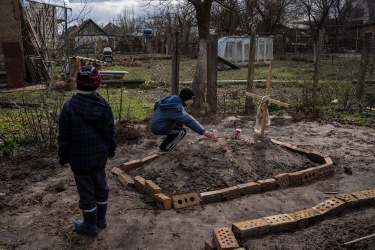 Der 10-jährige Vova Tanyuk (rechts) legt im Hof seines Hauses einen Orangensaft auf das Grab seiner Mutter Ira Tanyuk, die an den Folgen von Hunger und der Belastung durch den Krieg gestorben ist. Foto: dpa
