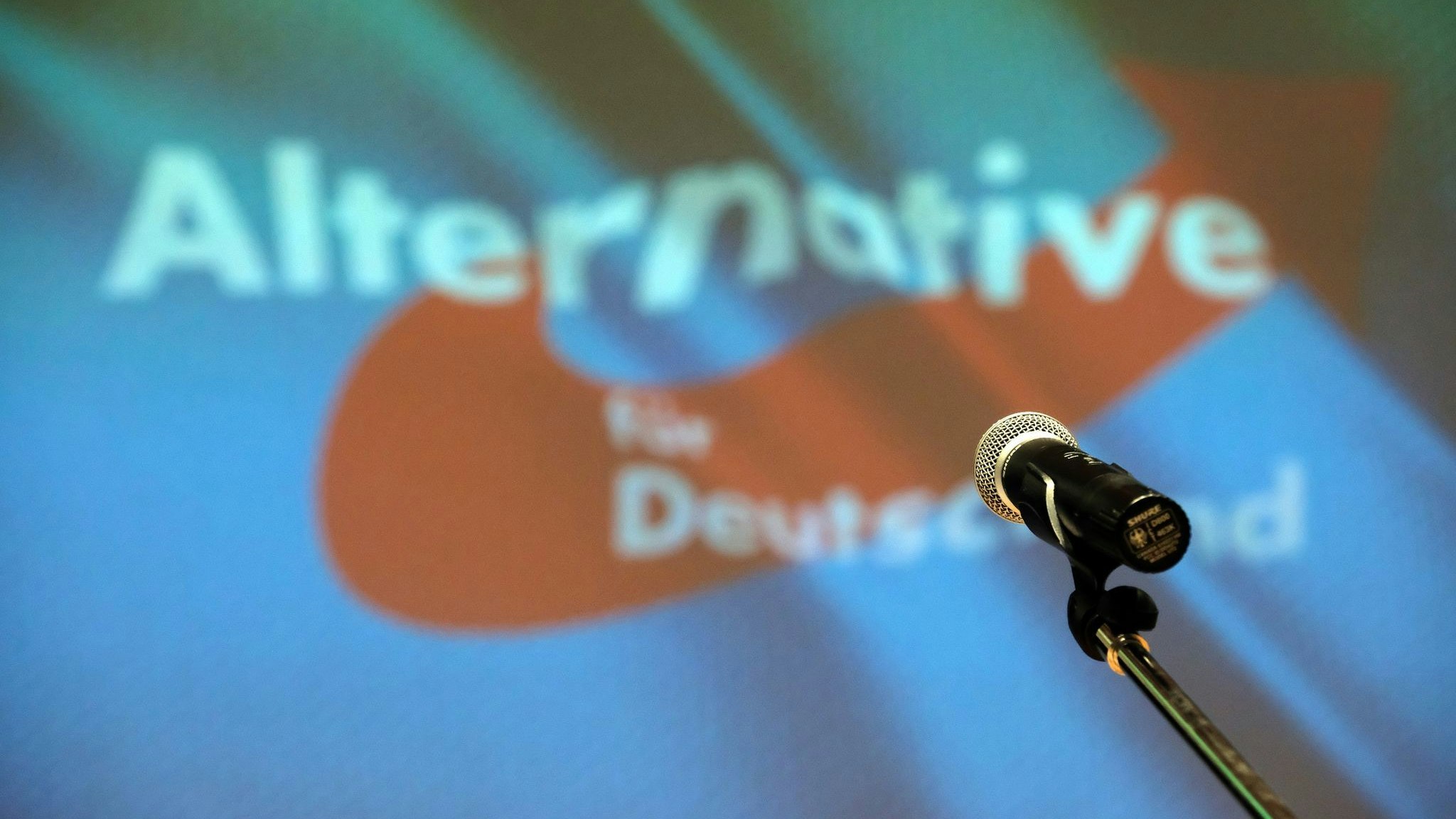 Ein Mikrofon steht auf der Bühne vor dem AfD-Partei-Logo. Foto: dpa/Willnow
