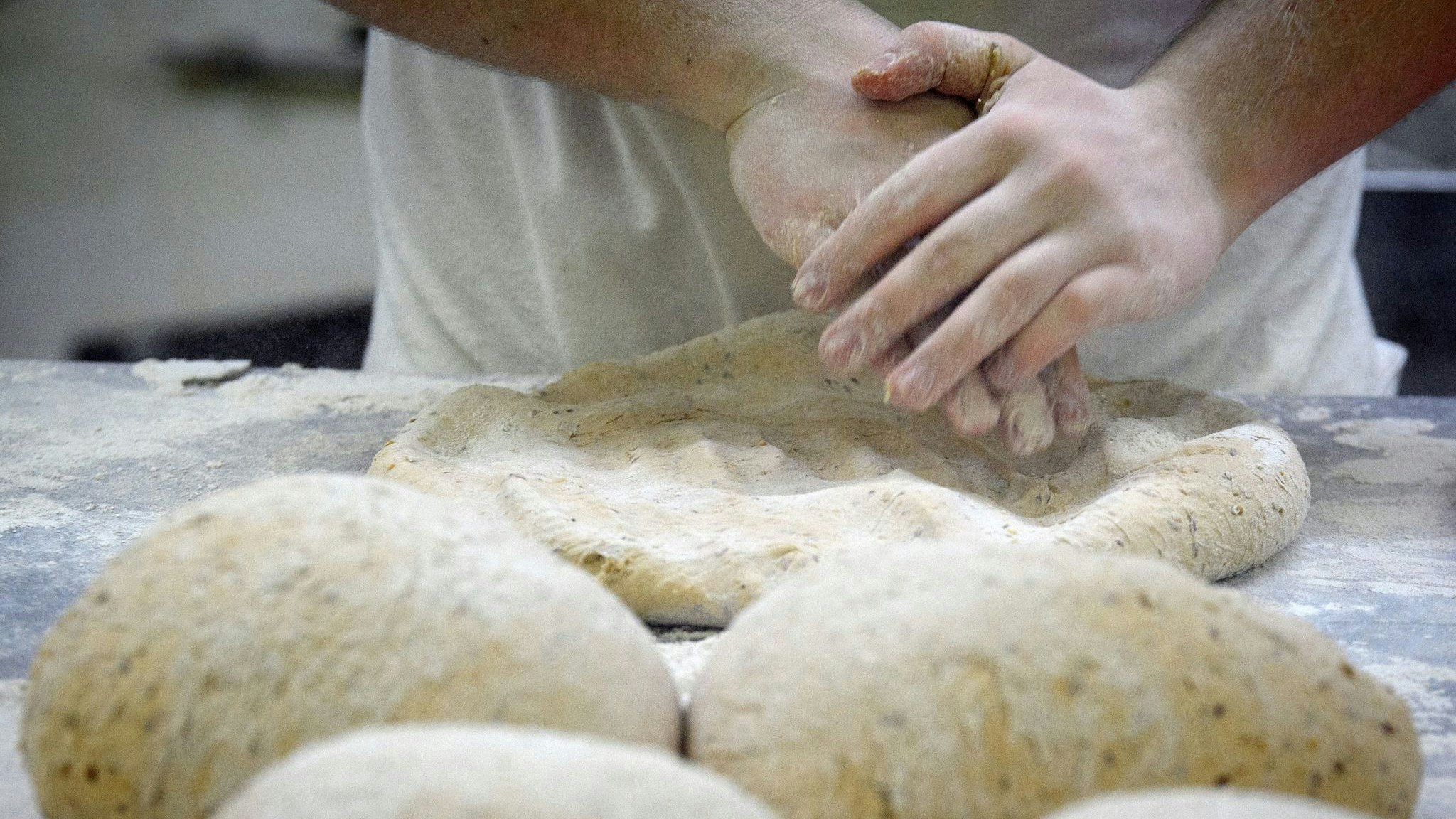 Ein Bäcker formt in der Backstube auf einer mit Mehl bestäubten Arbeitsplatte den Teig. Foto: dpa/Stache