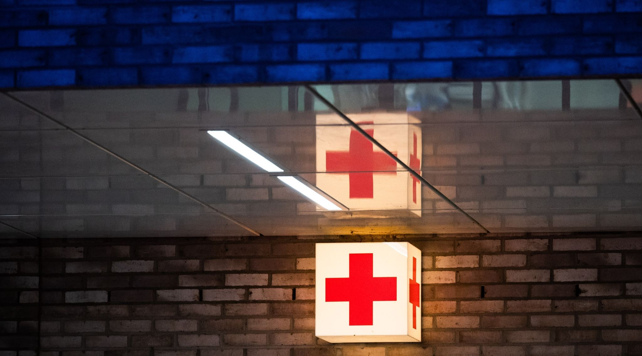Ein Leuchtkasten mit einem roten Kreuz hängt vor der Notaufnahme eines Krankenhauses. Foto dpa/Stratenschulte