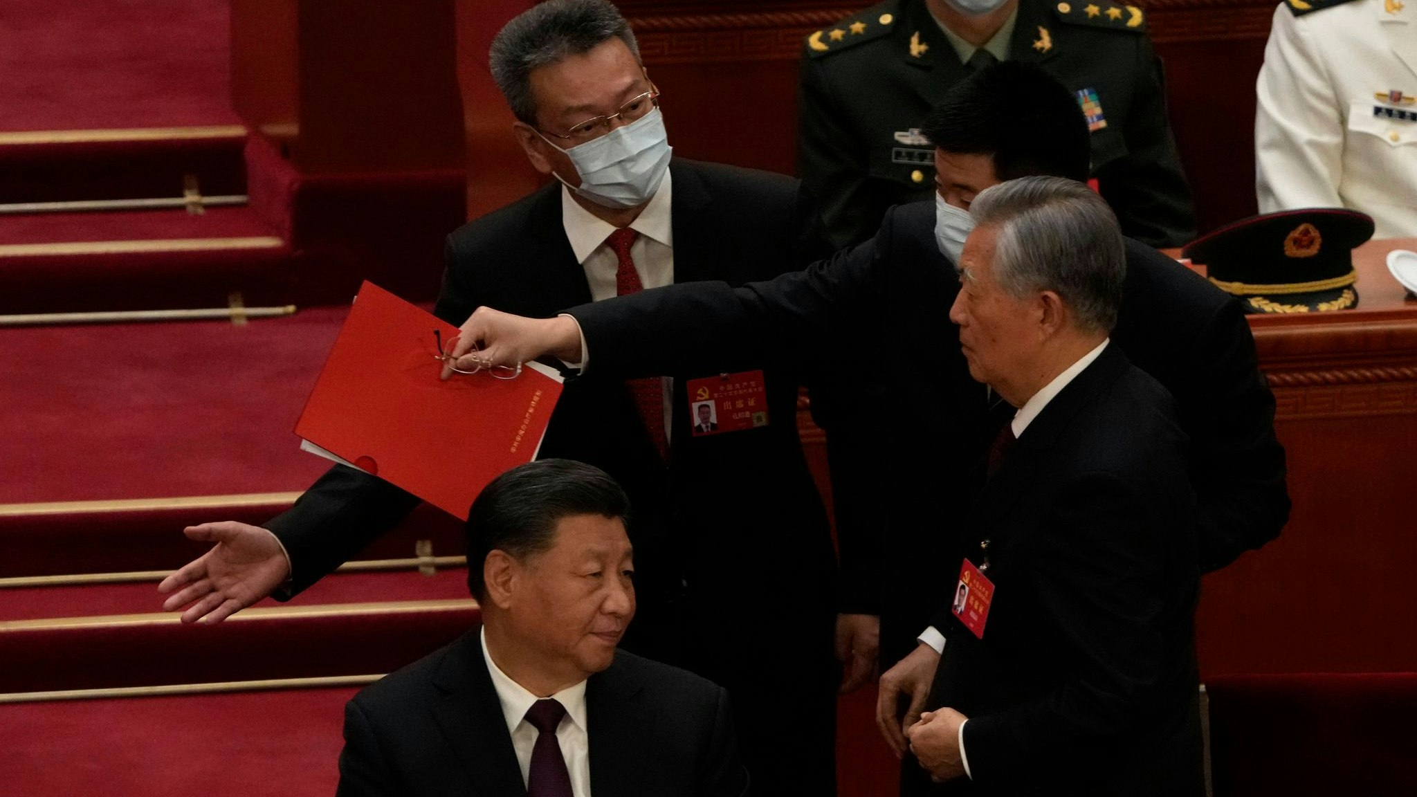 Chinas Ex-Präsident Hu Jintao (r) wird von seinem Platz weg begleitet. Links sitzt Xi Jinping und guckt zu. Foto: dpa/Ng Han Guan