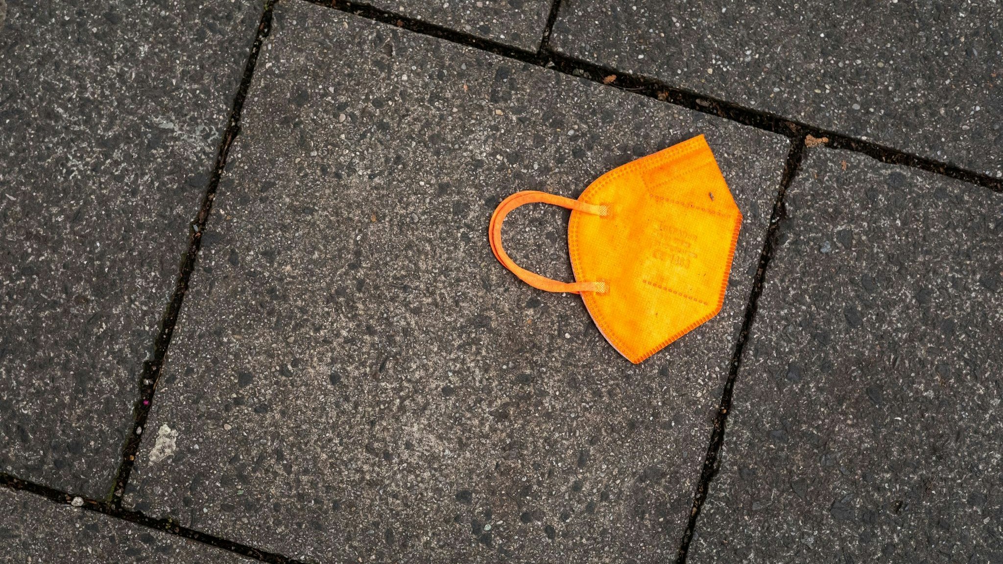 Ein gebrauchter orangefarbener Mund-Nasen-Schutz liegt auf dem Gehweg. Foto: dpa/Kneffel