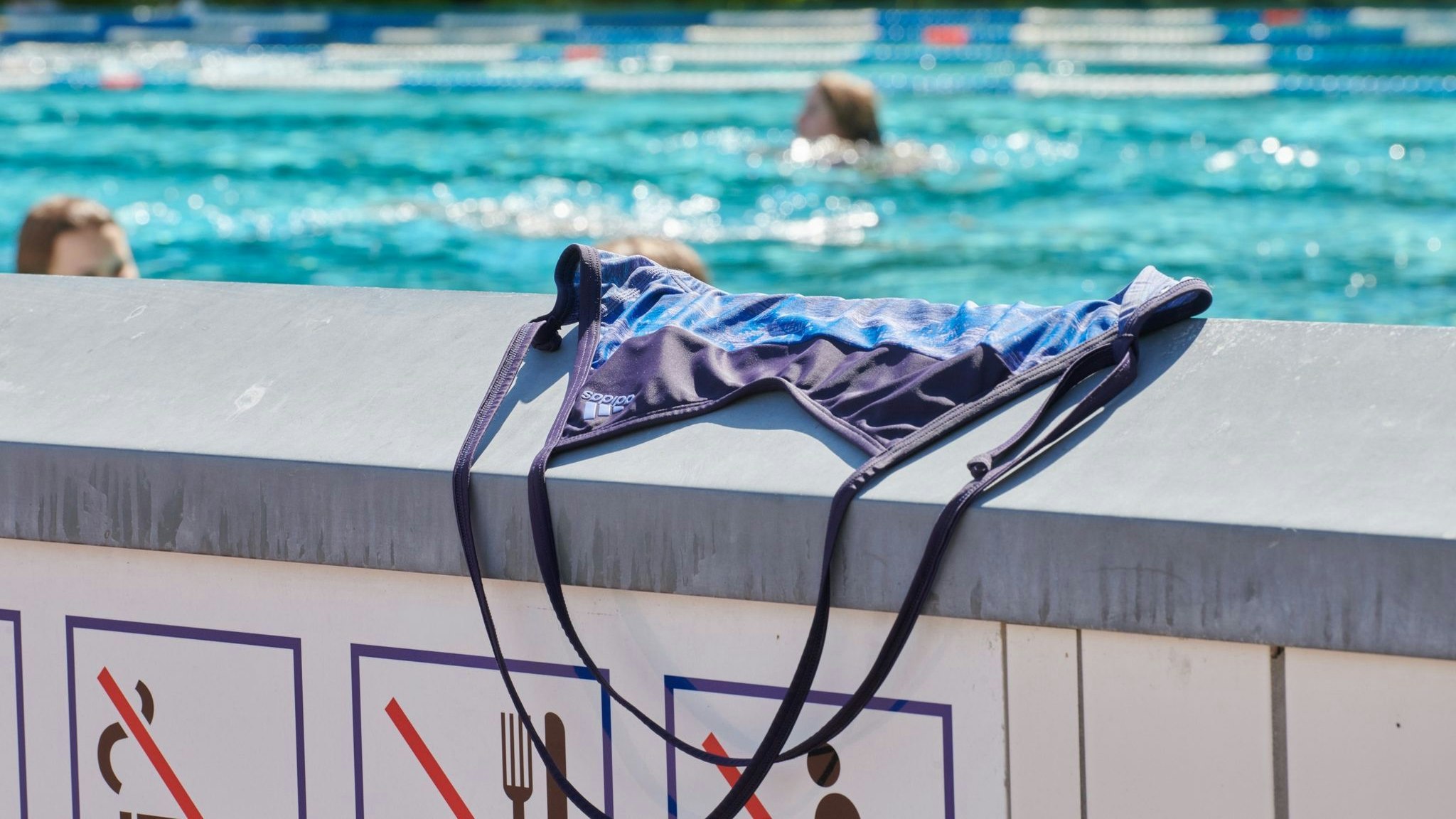 Ein Badeanzug liegt auf einer Mauer im Prinzenbad, dahinter schwimmen Menschen im Becken ihre Bahnen. Foto: dpa/Riedl