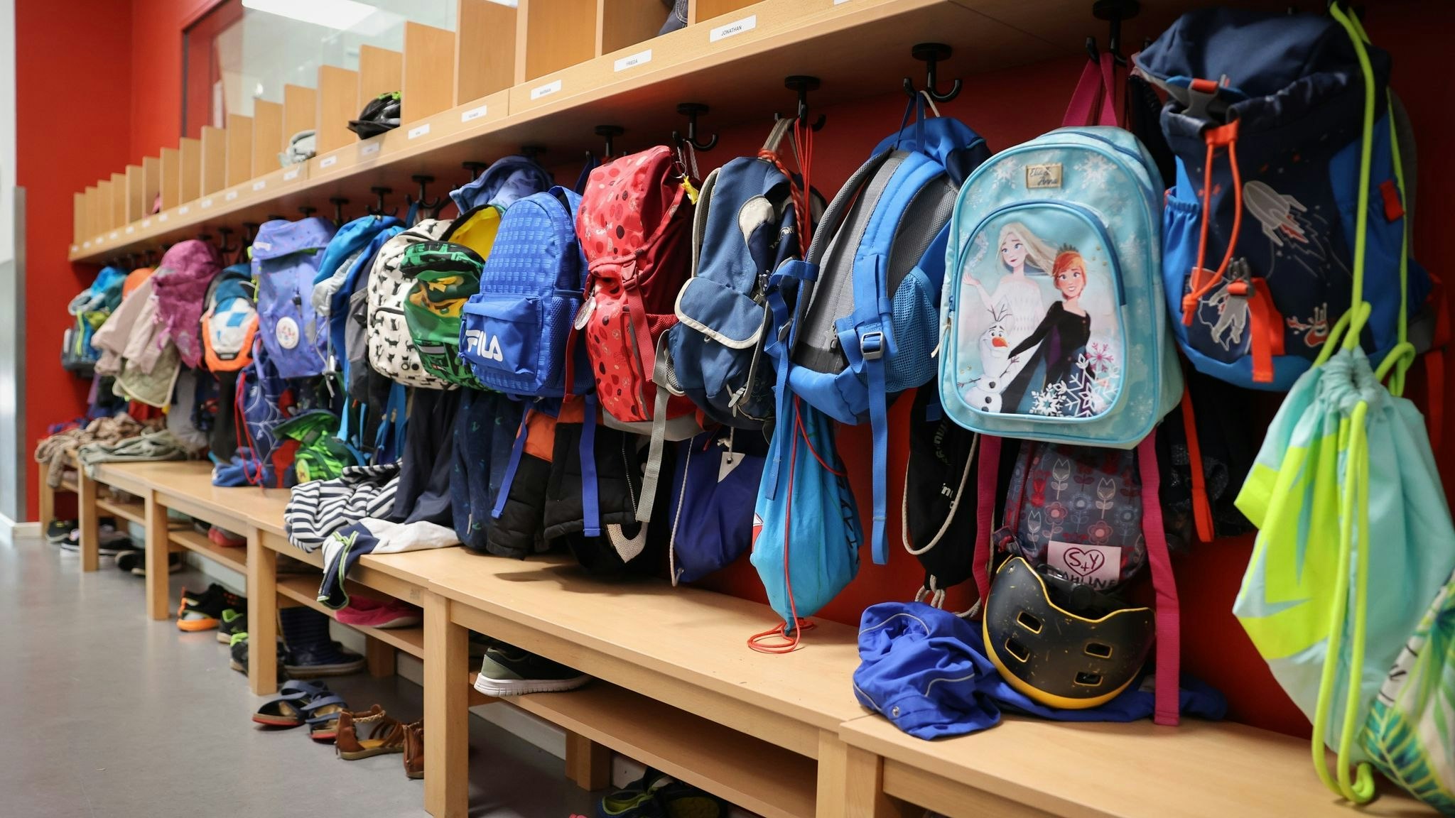 Sporttaschen und Schulranzen hängen an der Garderobe vor einem Klassenzimmer. Foto: dpa/Charisius