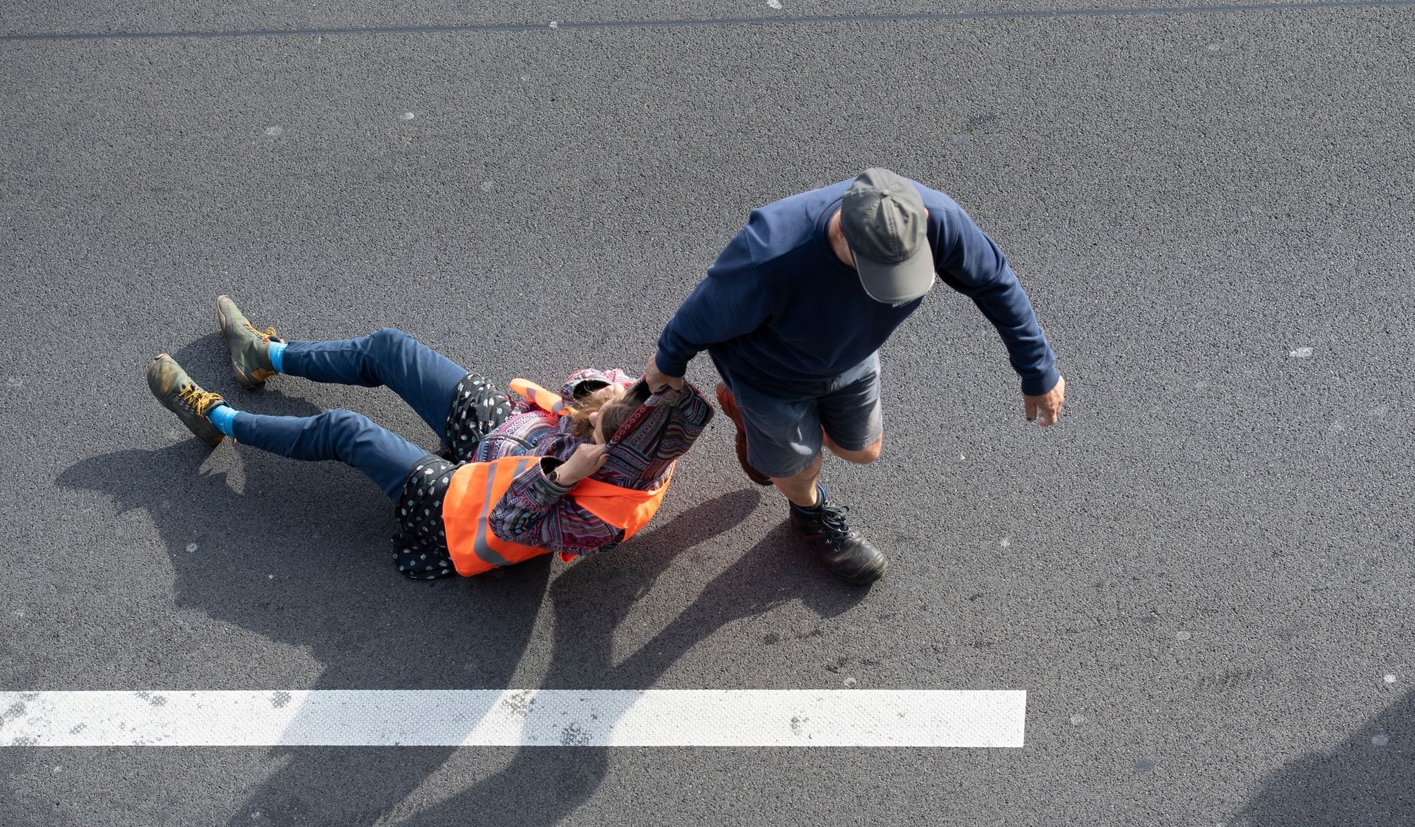 Ein Verkehrsteilnehmer (r) zieht bei einer Blockade der Letzten Generation auf der Autobahn 100 eine Aktivistin von der Straße. Erneut hat die Klimaaktivistengruppe an zahlreichen Stellen in der Stadt Straßen blockiert. Foto: dpa/Zinken