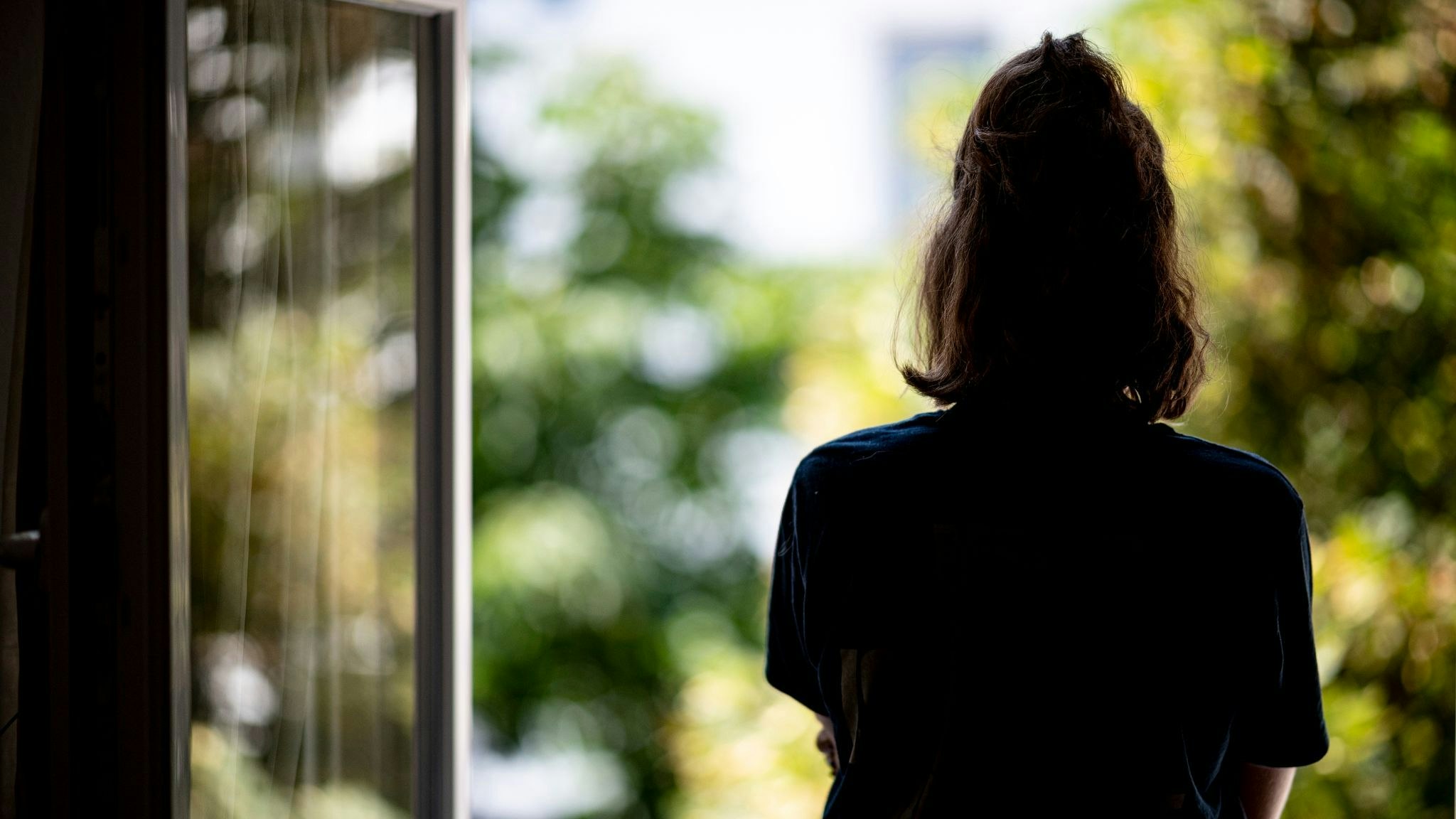 Eine Frau steht in ihrer Wohnung am Fenster. Foto: dpa/Sommer