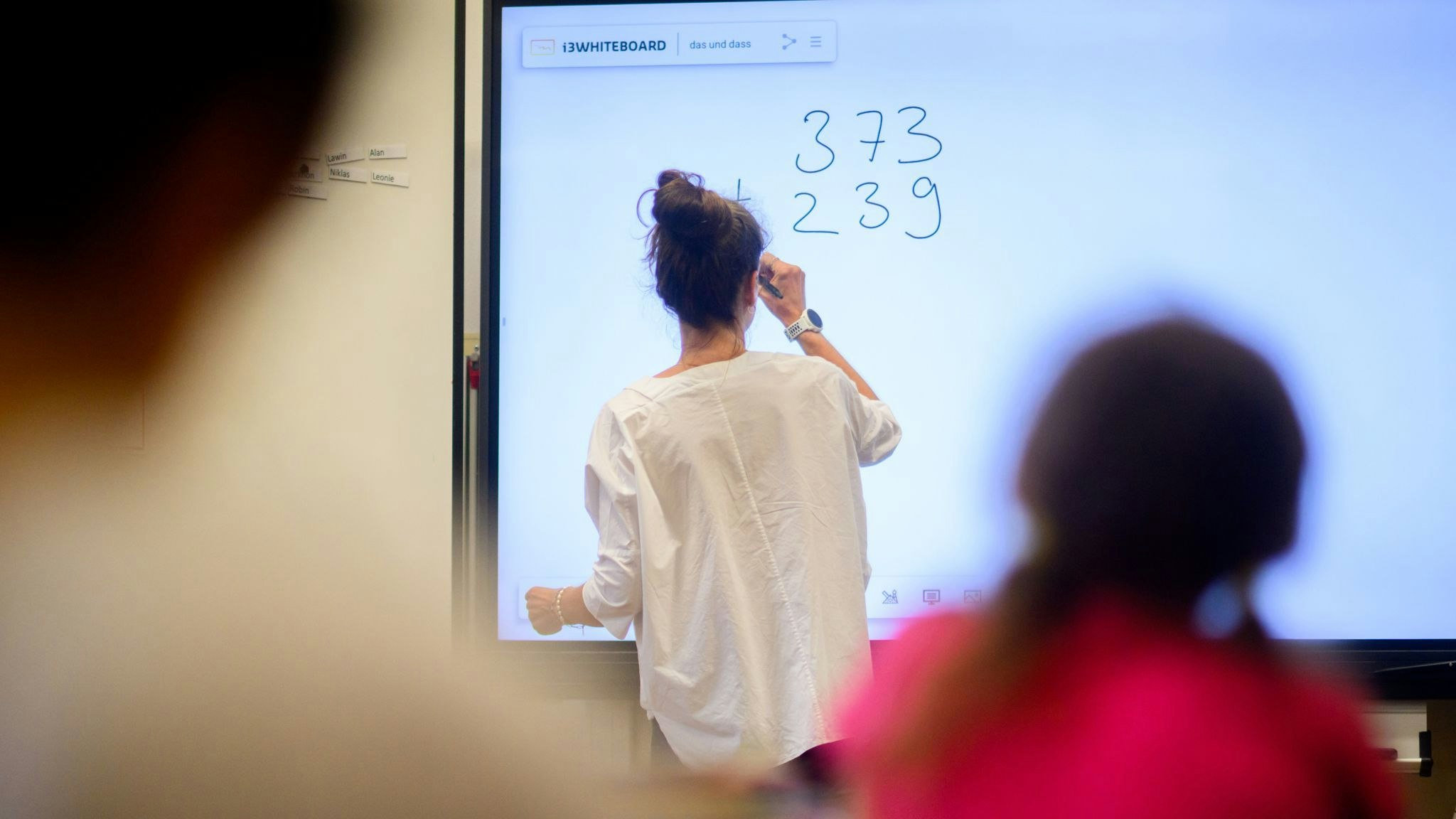 Ein Lehrerin schreibt eine Mathematikaufgabe auf eine digitale Schultafel im Klassenraum einer 4. Foto: dpa/Stratenschulte