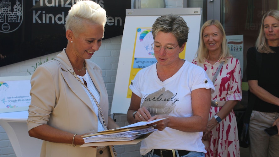 Silvia Breher (links) nimmt die gesammelten Unterschriften von Karin Möhlenkamp, Leiterin der Molberger Kita Die Arche, entgegen. Foto: Hoff