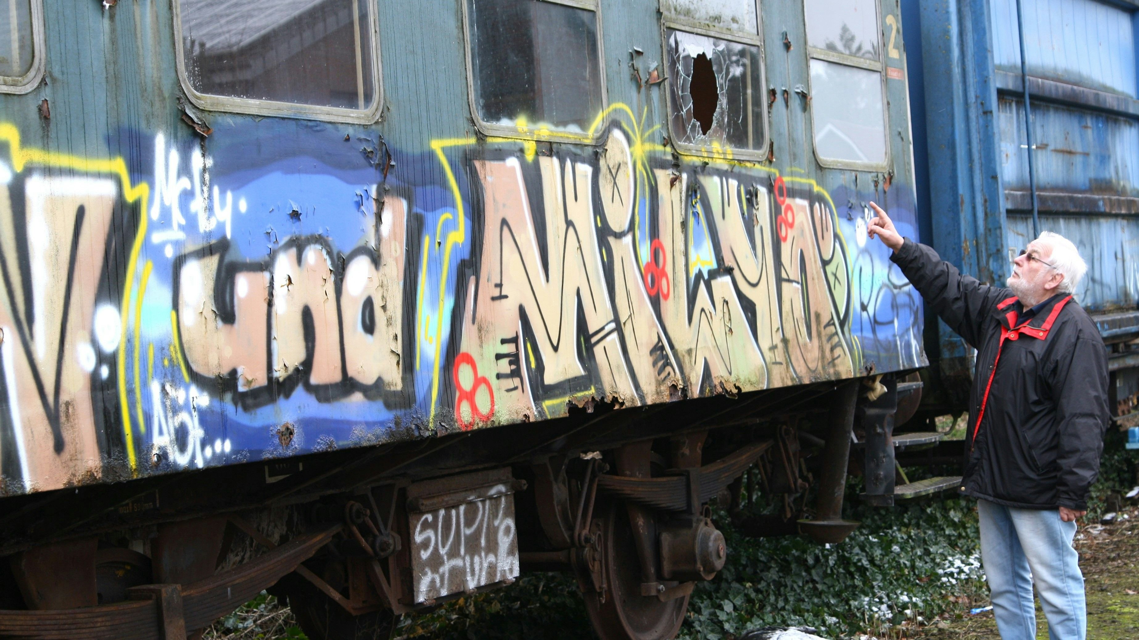 Ein fassungsloser Vorsitzender: Karl-Heinz Scholz zeigt auf die Graffitis und zertrümmerte Fenster im und am Wagon von 1923, der im Inneren jetzt vollkommen demoliert wurde. Foto: Pille