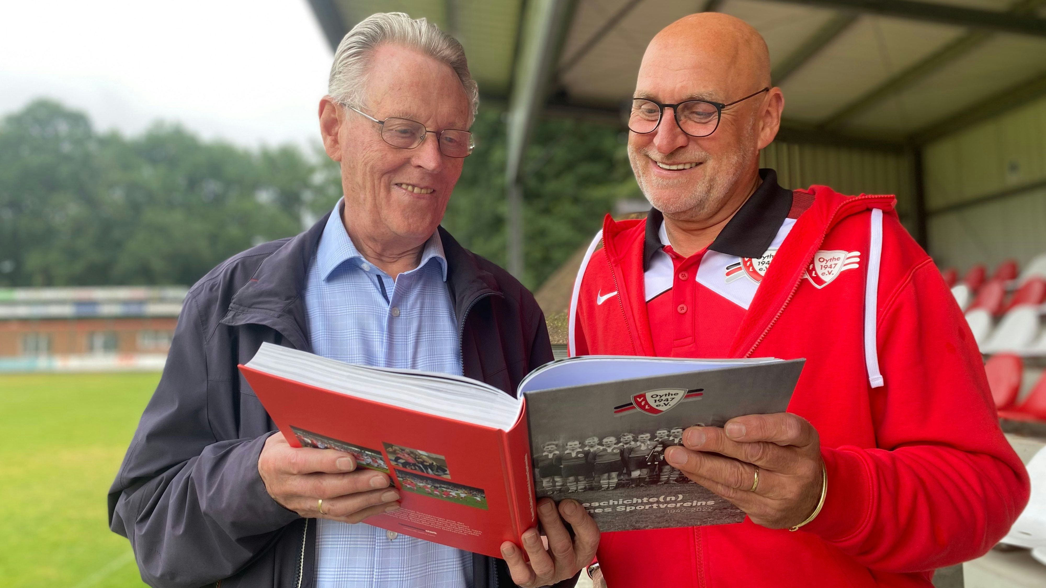Der 90-jährige Georg Rohenkohl (links) und Vorsitzender Hauke Anders blättern als Erste in dem Buch über 75 Jahre VfL Oythe. Foto: Freiwald