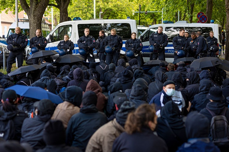 Demonstranten beteiligen sich an einer Sitzblockade an einer Zufahrt zum Schützenplatz. Foto: Moritz Frankenberg  dpa